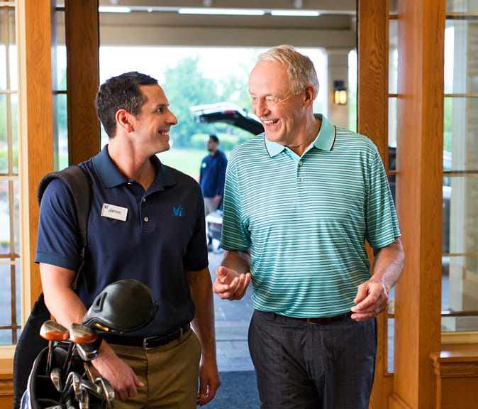 A man walks into the Vi at The Glen lobby chatting with an employee carrying golf clubs.